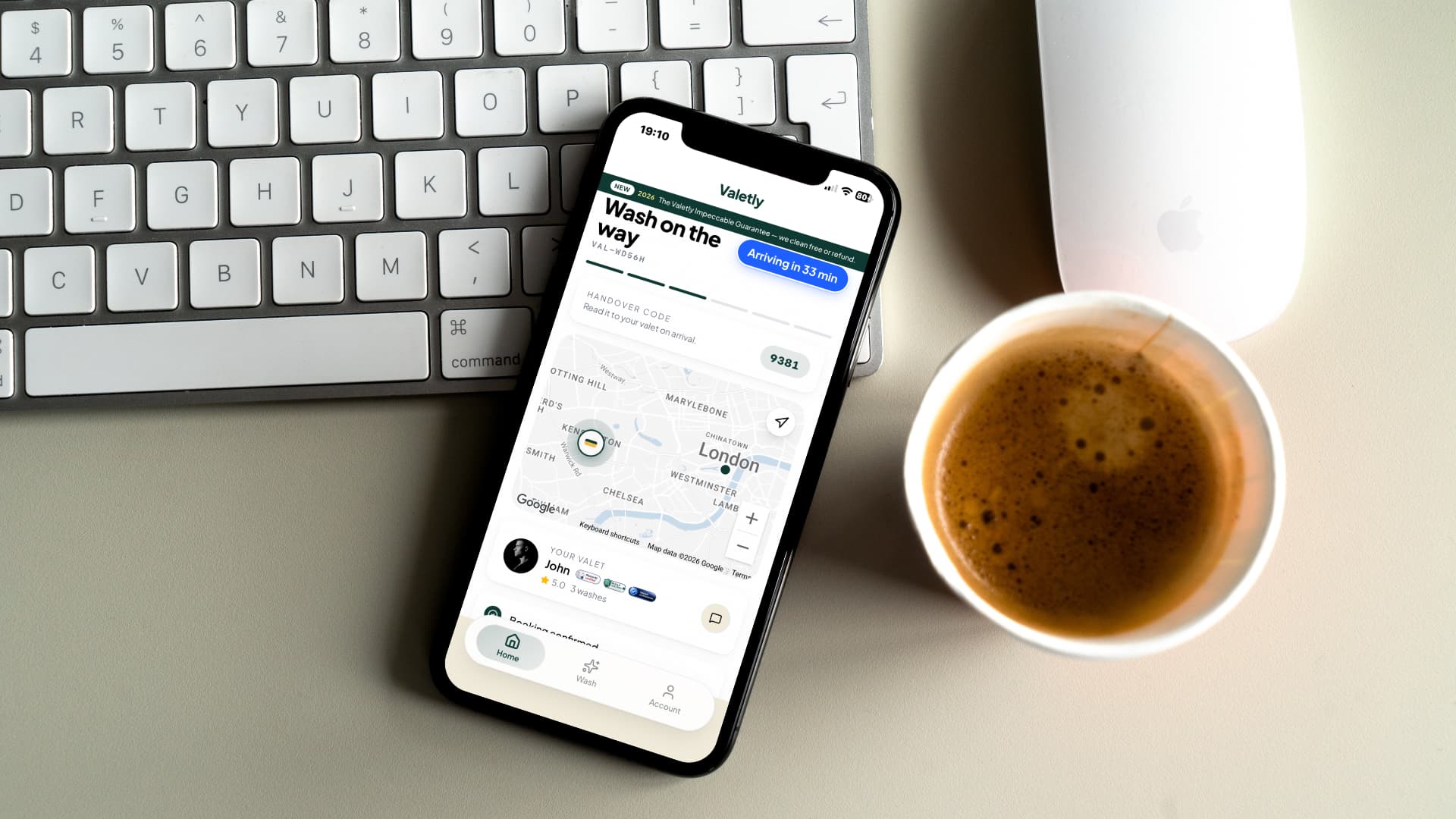 Valetly app tracking a car valet on an iPhone next to a keyboard and a coffee at the office